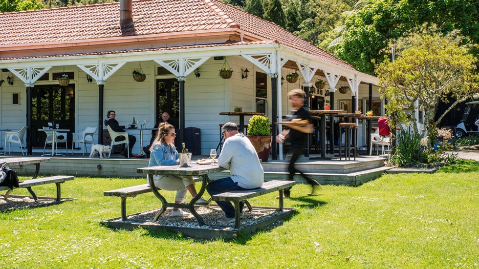 A couple sitting at the lawn picnic table receives food from a waiter in front of the Howden Homestead at the Furneaux Lodge Restaurant in the Marlborough Sounds at the top of New Zealand's South Island 