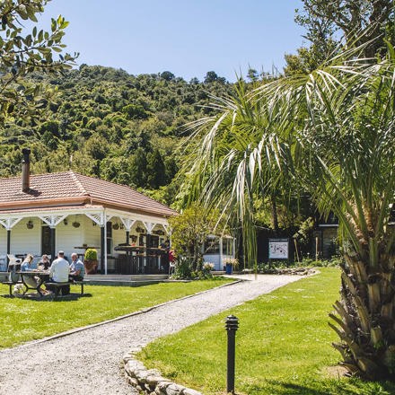 Guests dining outdoors at the lawn picnic tables in front of the Howden Homestead at the Furneaux Lodge Restaurant in the Marlborough Sounds at the top of New Zealand's South Island