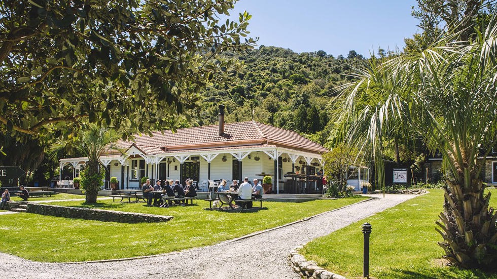 Guests dining outdoors at the lawn picnic tables in front of the Howden Homestead at the Furneaux Lodge Restaurant in the Marlborough Sounds at the top of New Zealand's South Island