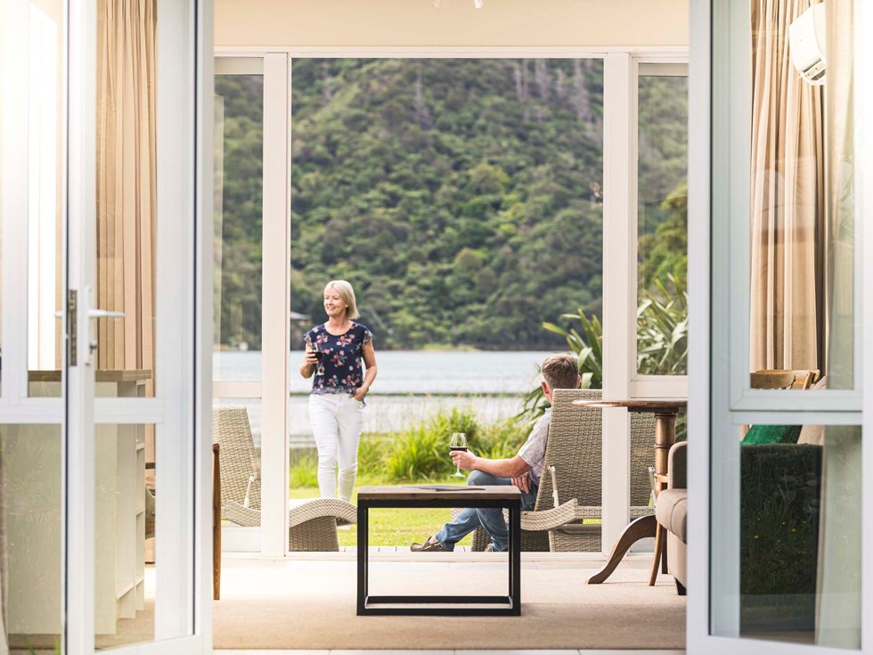 A couple enjoy glasses of wine on their private Endeavour Suite deck at Furneaux Lodge in the Marlborough Sounds at the top of New Zealand's South Island.