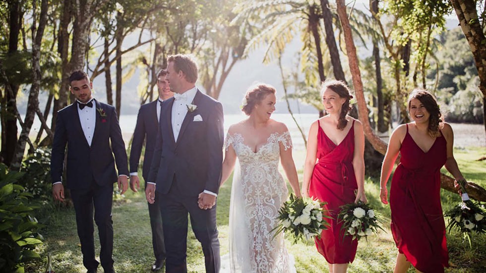 A bride, groom and wedding party walk through the native trees by the beach at Furneaux Lodge in the Marlborough Sounds in New Zealand's top of the South Island