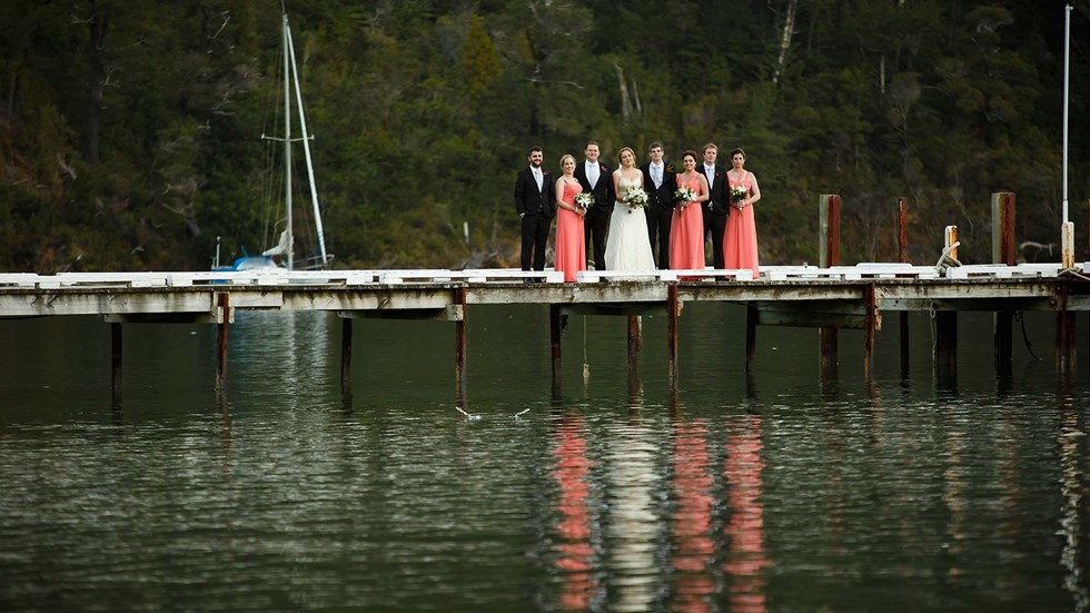 A bride, groom and wedding party stand on the Furneaux Lodge jetty in the Marlborough Sounds in New Zealand's top of the South Island