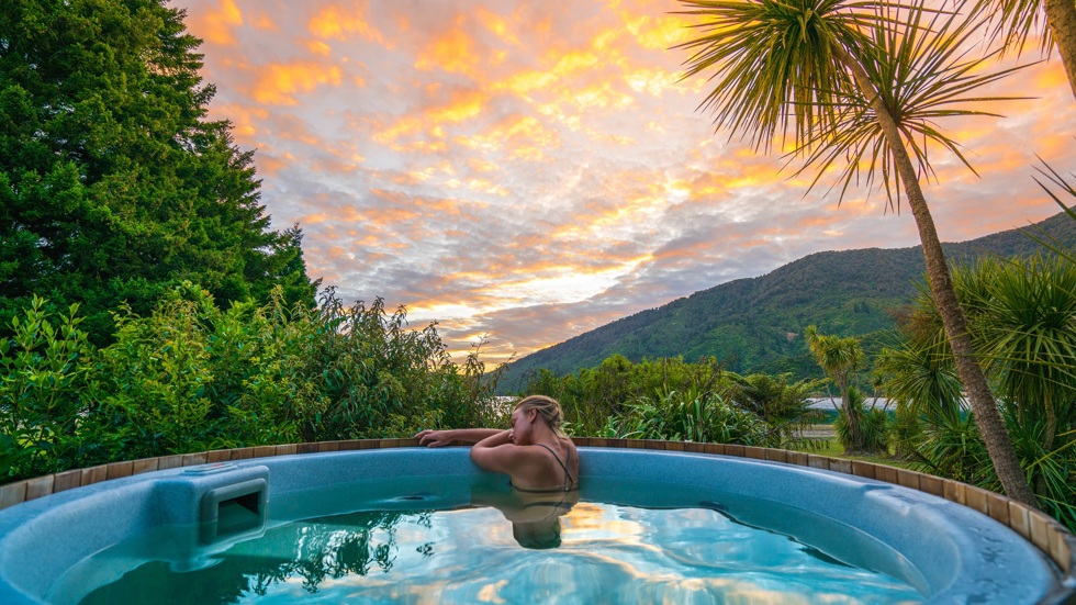 Woman relaxes in spa pool with sea view at sunset at Furneaux Lodge in New Zealand's Marlborough Sounds.