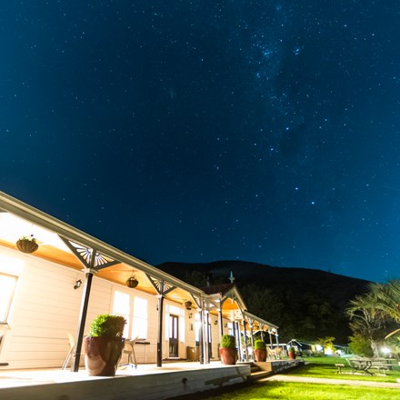 A view at night along the verandah of historic Howden House with lights on and stars in the sky, in the Marlborough Sounds at the top of New Zealand's South Island.