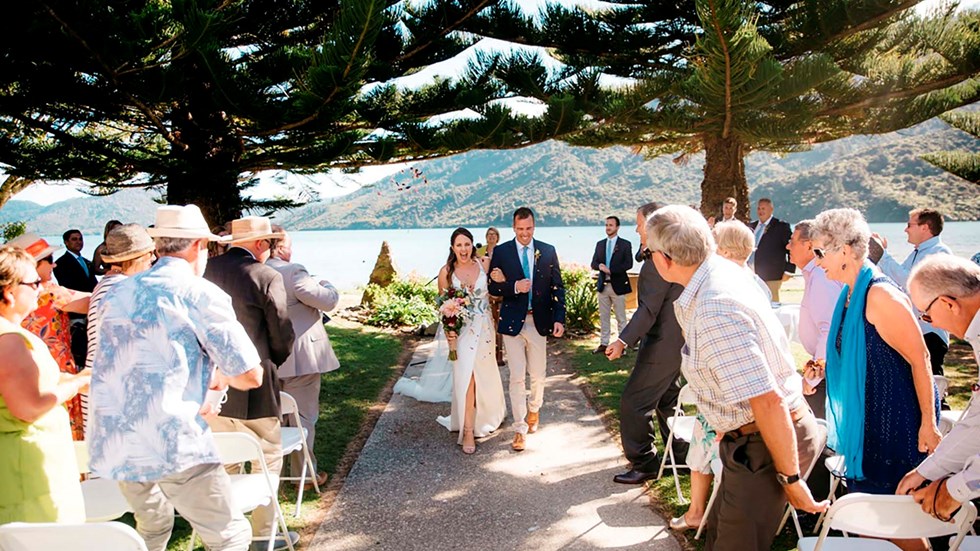 A newly married couple walk down the outdoor aisle through guests at Furneaux Lodge in the Marlborough Sounds in New Zealand's top of the South Island