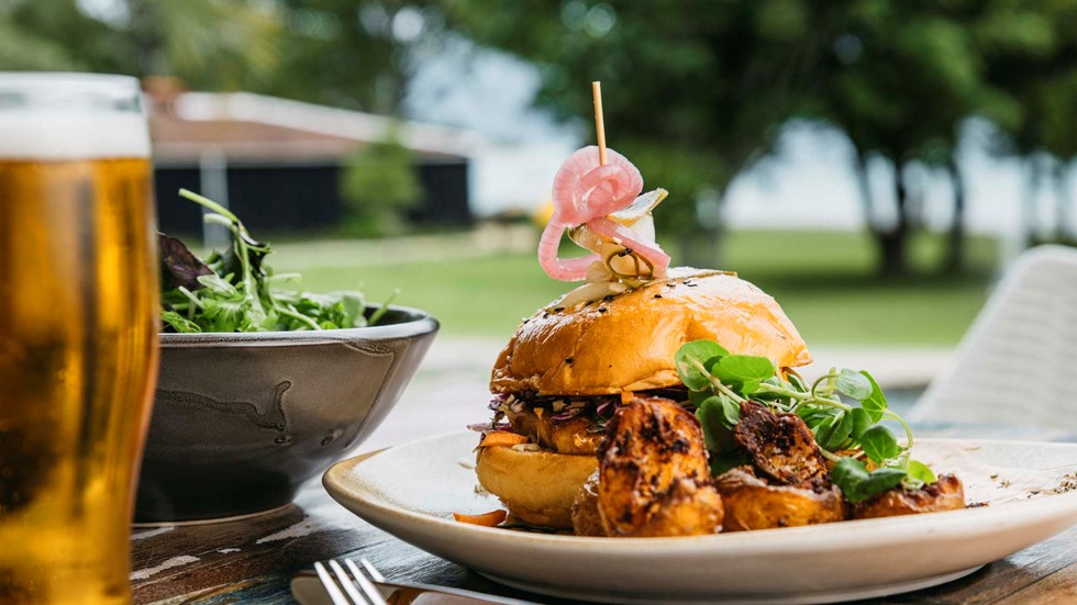 Gourmet chickpea and pumpkin burger with potatoes and side salad served with ocean view and a pint of beer at the Furneaux Lodge Restaurant in the Marlborough Sounds at the top of New Zealand's South Island.