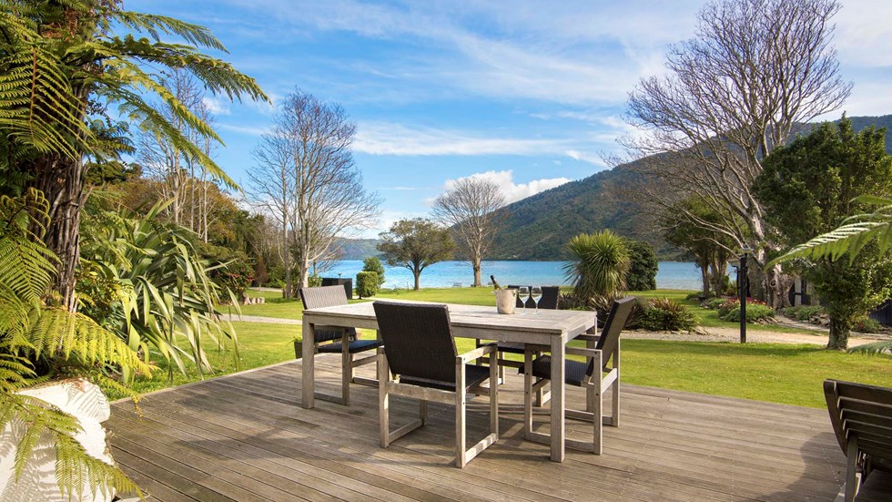 An outdoor dining table on a private Cook's Cottage deck overlooking the Endeavour Inlet Bay at Furneaux Lodge in the Marlborough Sounds at the top of New Zealand's South Island.