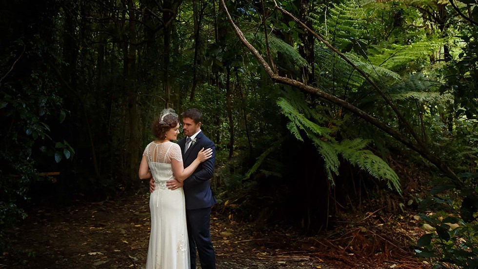 A bride and groom embrace surrounded by lush native green bush at Furneaux Lodge in the Marlborough Sounds in New Zealand's top of the South Island