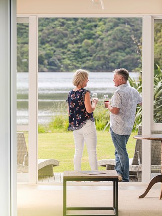 A couple enjoying glasses of Pinot Noir outside on an Endeavour Suite Rows of wine glasses on a shelf at the Furneaux Lodge  in the Marlborough Sounds at the top of New Zealand's South Island.