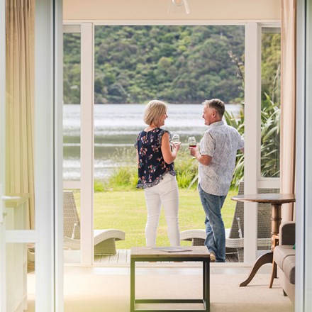A couple enjoying glasses of Pinot Noir outside on an Endeavour Suite Rows of wine glasses on a shelf at the Furneaux Lodge  in the Marlborough Sounds at the top of New Zealand's South Island.