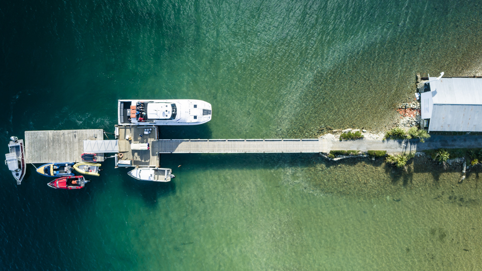 Aerial view looking down at the Furneaux Lodge jetty with lots of small boats and a Cougar Line vessel, in the Marlborough Sounds at the top of New Zealand's South Island.