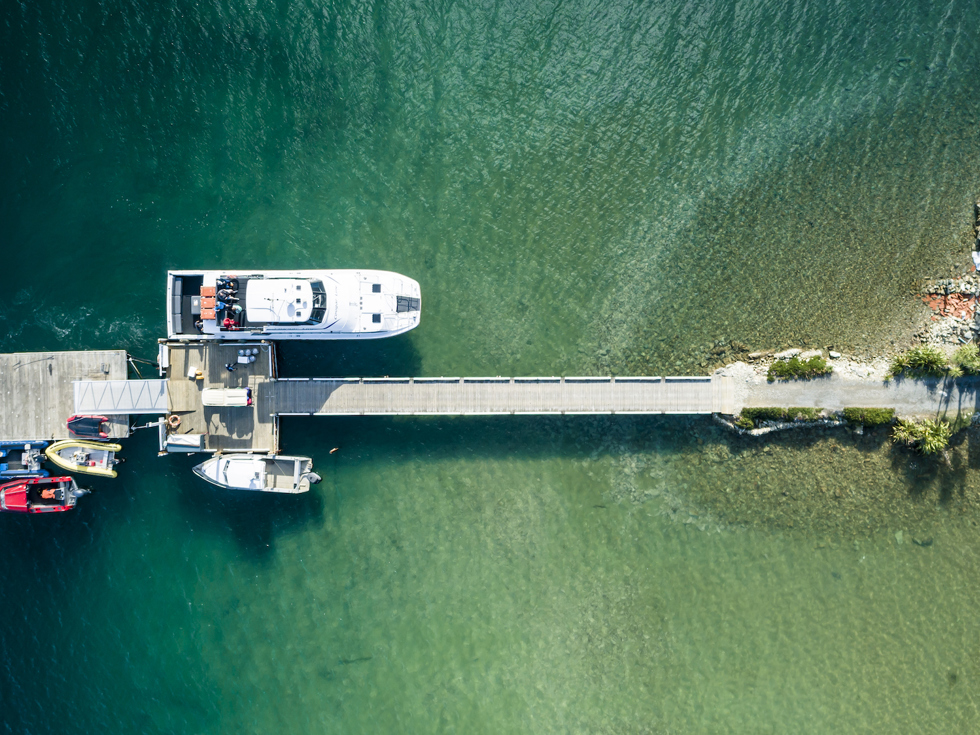 Aerial view looking down at the Furneaux Lodge jetty with lots of small boats and a Cougar Line vessel, in the Marlborough Sounds at the top of New Zealand's South Island.