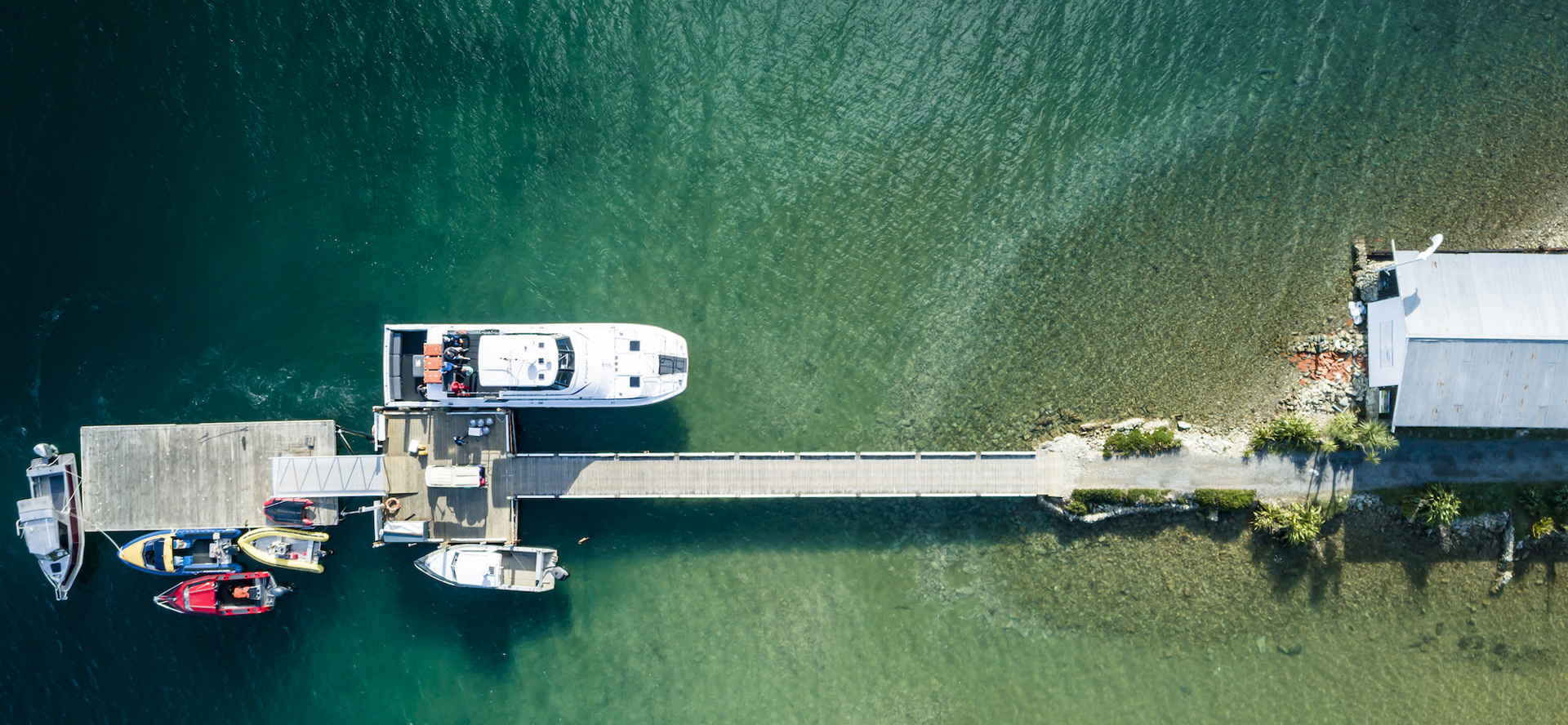 Aerial view looking down at the Furneaux Lodge jetty with lots of small boats and a Cougar Line vessel, in the Marlborough Sounds at the top of New Zealand's South Island.